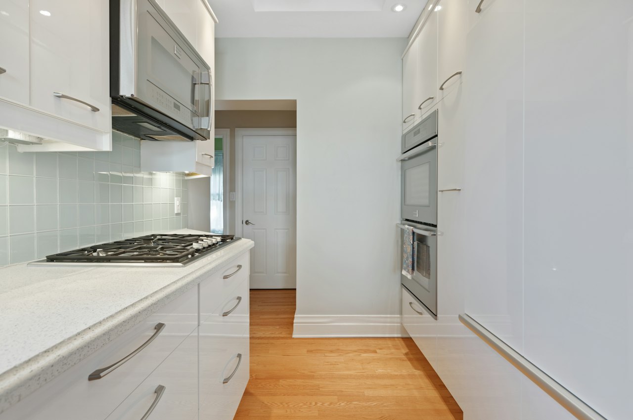 Aménagement d'une petite cuisine en longueur avec meubles blancs, plan de travail continu et plaque de cuisson